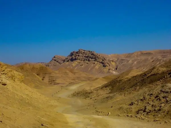 Wüstenlandschaft mit sandigen Hügeln und einem markanten Felsen im Hintergrund