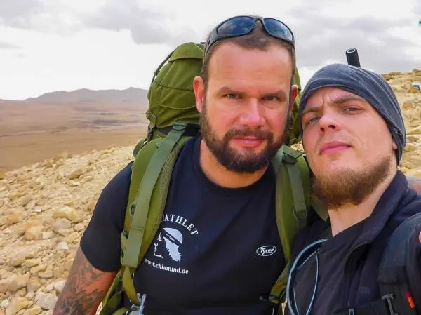 Zwei Personen mit Rucksäcken stehen auf einem felsigen Hang