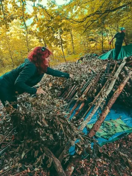 Frau deckt eine selbstgebaute Notunterkunft mit Ästen und Blättern ab