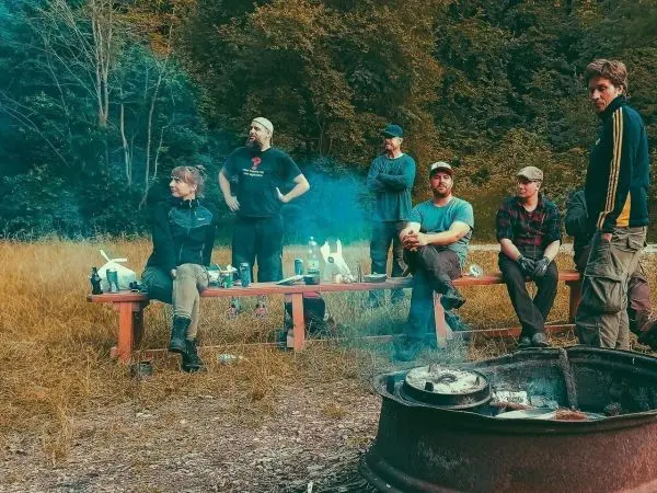 Gruppe sitzt auf einer Bank neben einem Lagerfeuer mit Rauchentwicklung