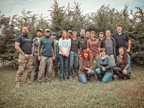 Gruppe von 16 Personen vor einer Hecke im Freien