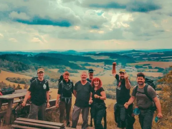 Gruppe von Wanderern posiert auf einem Aussichtspunkt mit Rucksäcken und lächelt