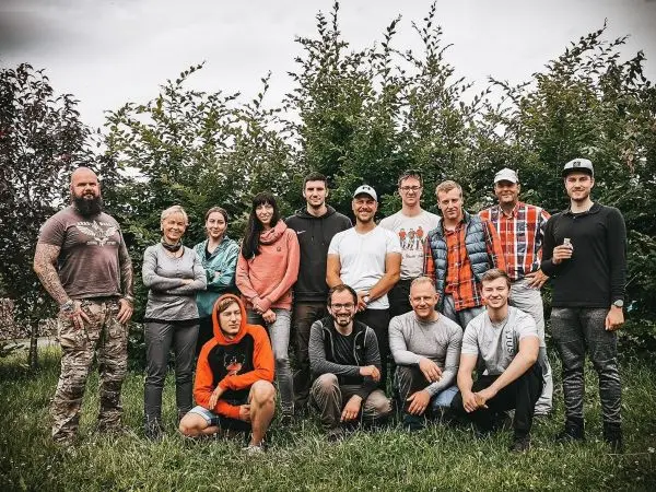 Gruppenszenario mit mehreren Personen vor einer Hecke, alle stehen oder sitzen