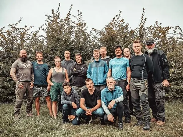 Gruppierung von 15 Personen in Outdoor-Bekleidung vor einer Hecke