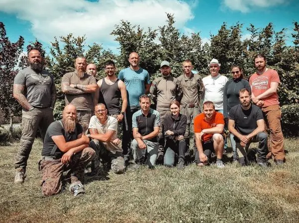 Gruppierung von 16 Personen im Freien, umgeben von Bäumen und Gras