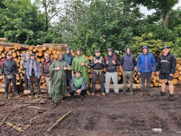 Gruppierung von Personen vor einem Holzstapel, einige tragen Regenjacken