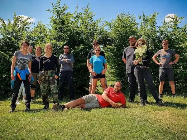 Gruppierung von zehn Personen im Freien vor einer Hecke, einige halten Pflanzen