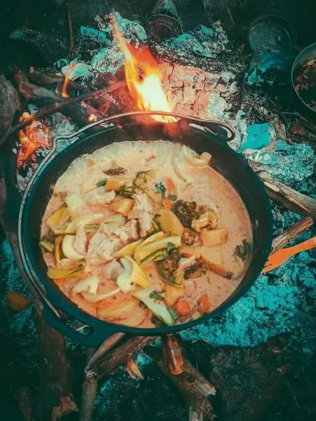 Kessel mit Gemüse und Fleisch über offenem Feuer auf Holzscheiten