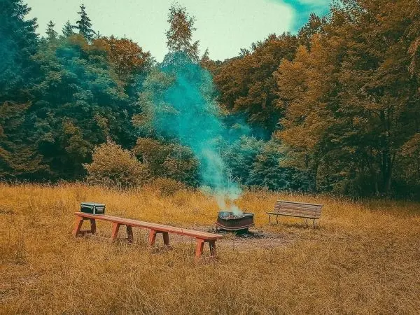 Lagerfeuer mit Rauch, Bank und Holzbank im Gras