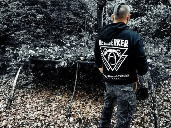 Mann steht vor einer selbstgebauten Tarp-Notunterkunft im Wald