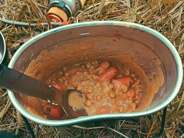 Topf mit Eintopf und Löffel auf dem Boden, umgeben von Gras