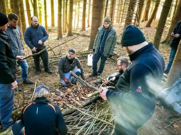 Gruppe von Personen arbeitet an einem Lager aus Ästen im Wald beim Survival Training