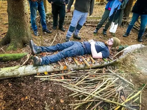 Improvisierte Trage aus Ästen mit liegender Person im Wald