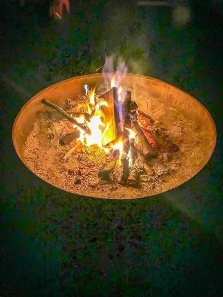 Kleine Flamme brennt in einer runden Feuerstelle mit Holzstücken