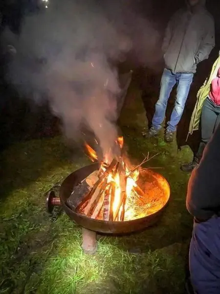 Kleine Flamme mit Rauch aus einem Feuerkorb, umgeben von Personen