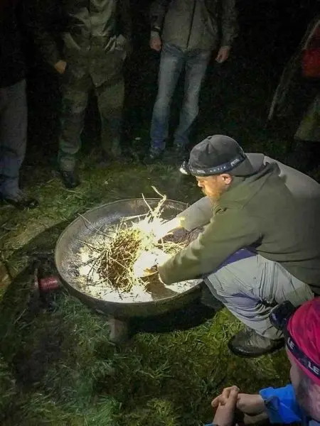 Person entzündet Zweige in einer Feuerschale beim Survival Training