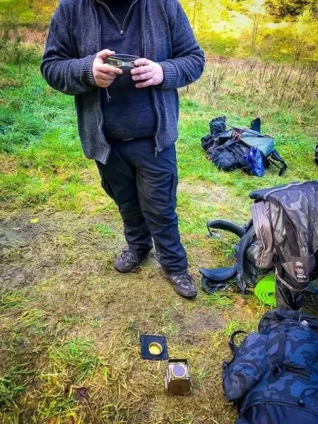 Person hält ein Gerät in der Hand, während ein Kocher auf dem Boden steht