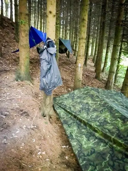 Tarp-Notunterkunft und Jacke hängen an Bäumen im Wald