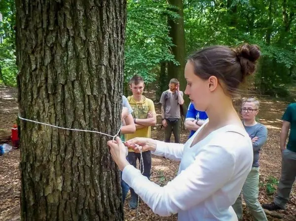 Frau bindet eine Schnur um einen Baumstamm, während andere zuschauen