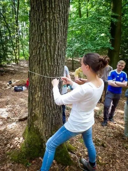 Frau spannt ein Seil um einen Baumstamm im Wald