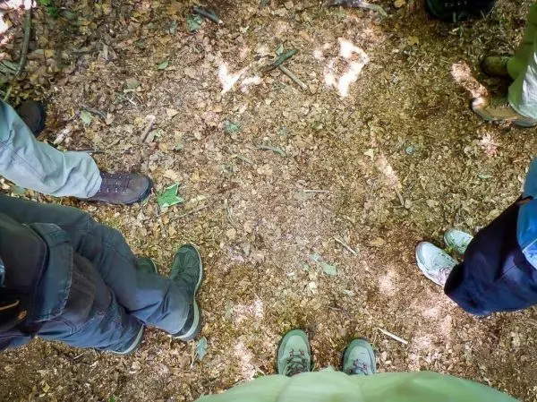 Füße verschiedener Schuhe stehen auf einem mit Laub bedeckten Waldboden
