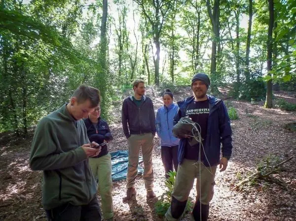 Gruppe steht im Wald, einige halten Ausrüstung in den Händen