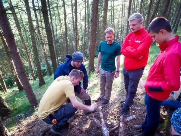 Gruppe von Personen beobachtet einen anderen beim Arbeiten mit Holz im Wald