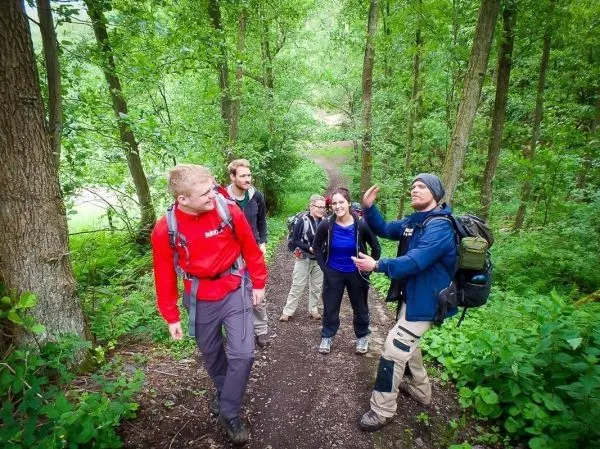 Gruppe von Wanderern auf einem Waldweg, einige tragen Rucksäcke und diskutieren