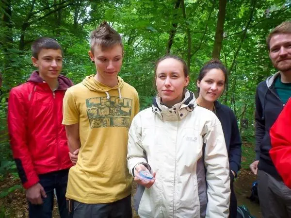 Gruppierung von fünf Personen im Wald, eine Person hält einen Gegenstand in der Hand