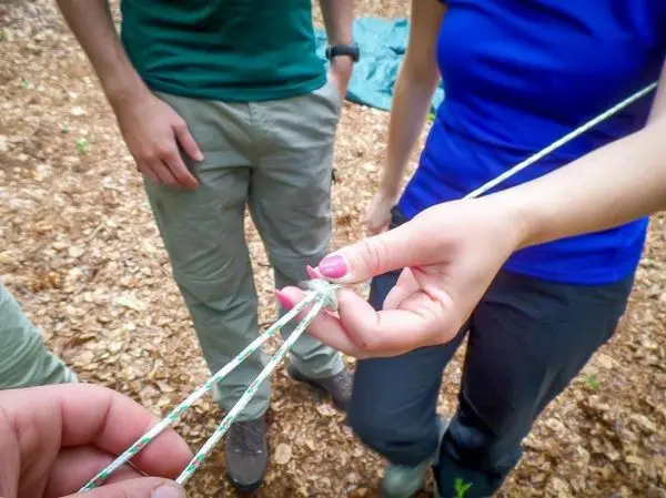 Hände binden ein Seil mit einem Knoten in einem Waldgebiet