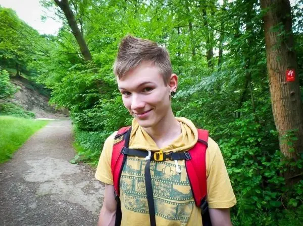 Junger Mann mit Rucksack steht auf einem Waldweg umgeben von Bäumen