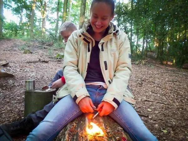 Kleine Flamme auf Holzstück, Zunder wird bearbeitet