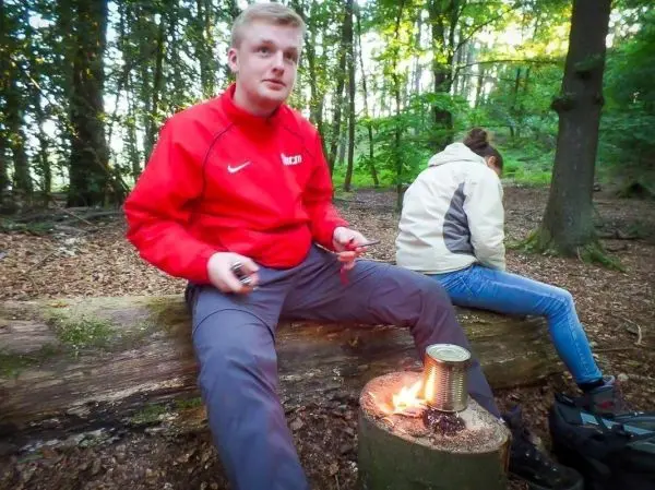 Kleine Flamme brennt auf einem Holzstück neben einem Kochtopf