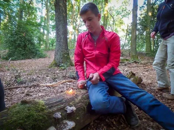 Kleines Bodenfeuer brennt auf einem Baumstamm, während jemand mit einem Messer arbeitet