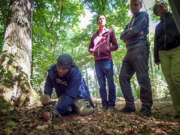 Mann bearbeitet Zunder mit einem Messer, während andere zuschauen