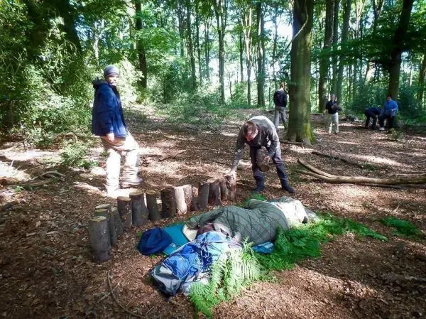 Mann bereitet Schlafplatz mit Decke und Rucksack im Wald vor
