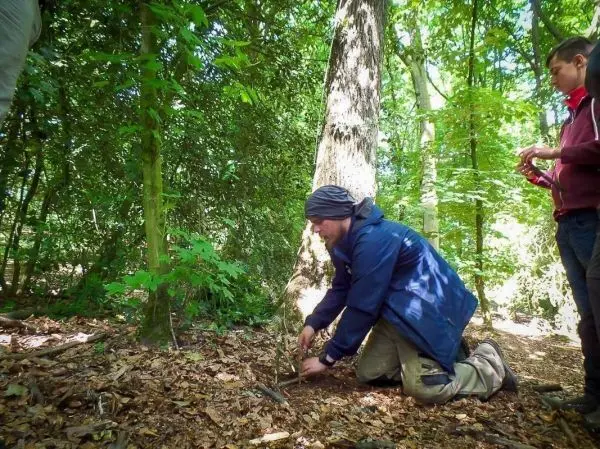 Mann kniet im Wald und baut eine Schlagfalle aus Ästen