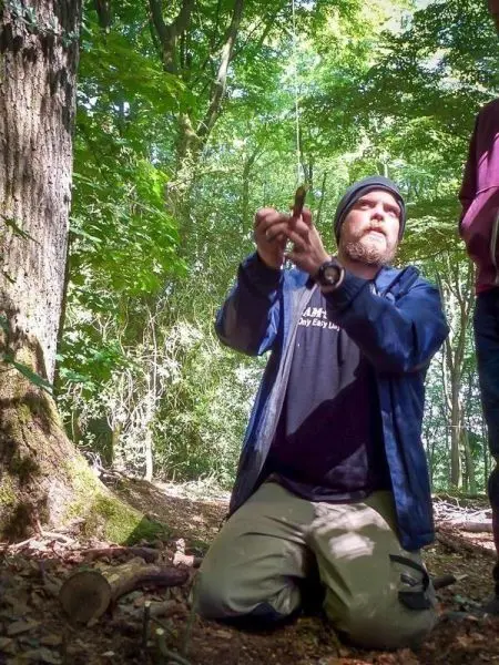 Mann kniet im Wald und bereitet eine selbstgebaute Schlagfalle vor