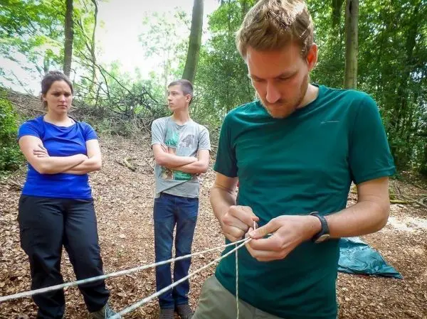Mann knotet Seil, während zwei Personen im Hintergrund beobachten