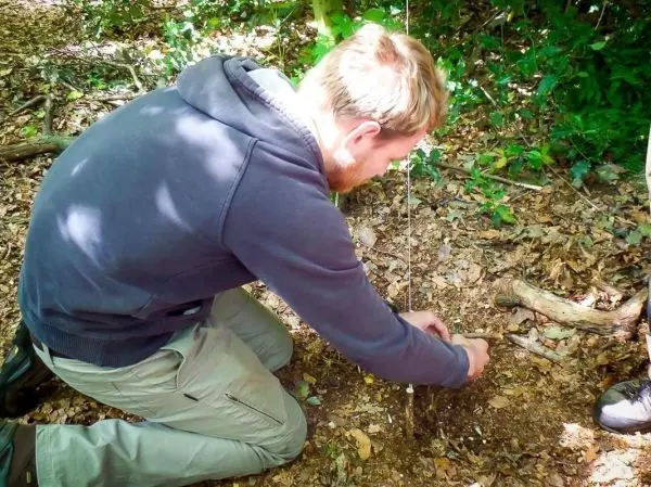 Mann richtet eine selbstgebaute Schlagfalle im Wald ein