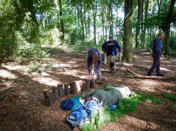 Mann spaltet Holzstücke mit einer Axt im Wald, während andere sich umsehen