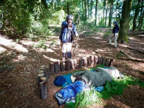 Mann steht neben einer Holzbarriere, während eine Person auf einer Isomatte liegt