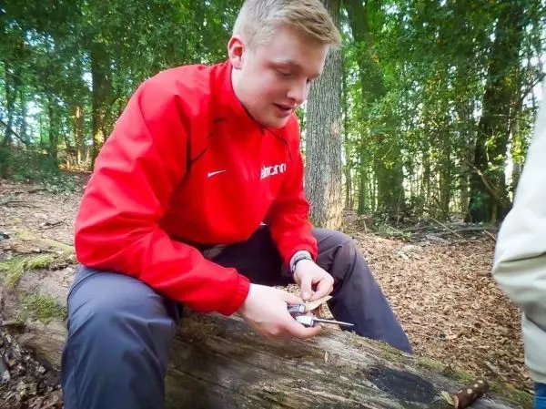 Messer schneidet Holzstück auf umgefallenem Baumstamm im Wald