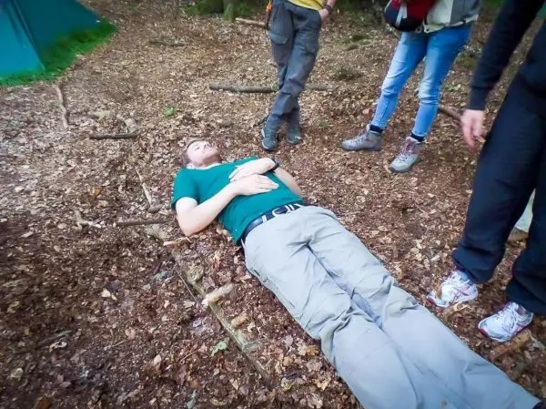 Person liegt auf dem Boden im Wald, umgeben von anderen Personen