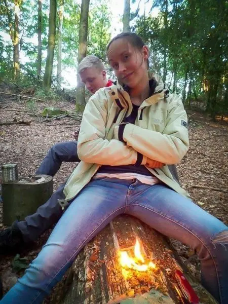 Person sitzt auf einem Baumstamm und schaut in die Kamera