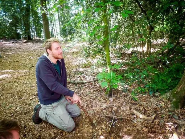 Person sitzt im Wald und zeigt auf eine selbstgebaute Falle