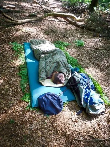 Schlafsack auf Isomatte im Wald, daneben Rucksack und weitere Ausrüstung
