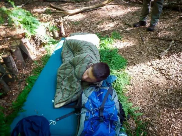 Schlafsack liegt auf einer Isomatte im Wald, Rucksack daneben