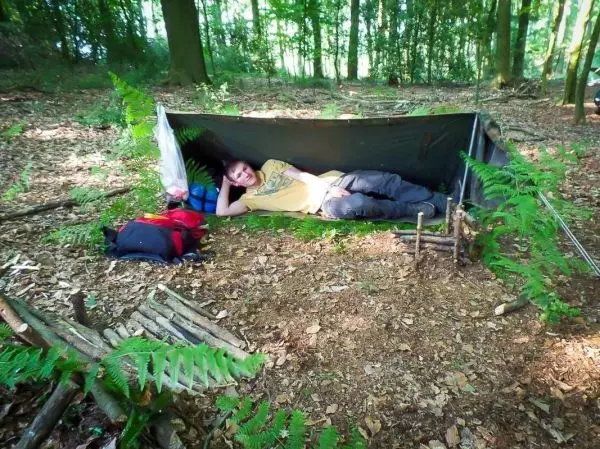 Tarp-Notunterkunft aus Plane und Ästen mit Gepäck im Hintergrund