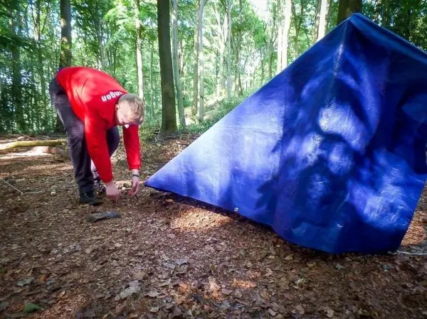 Tarp-Notunterkunft wird mit Heringen im Boden befestigt